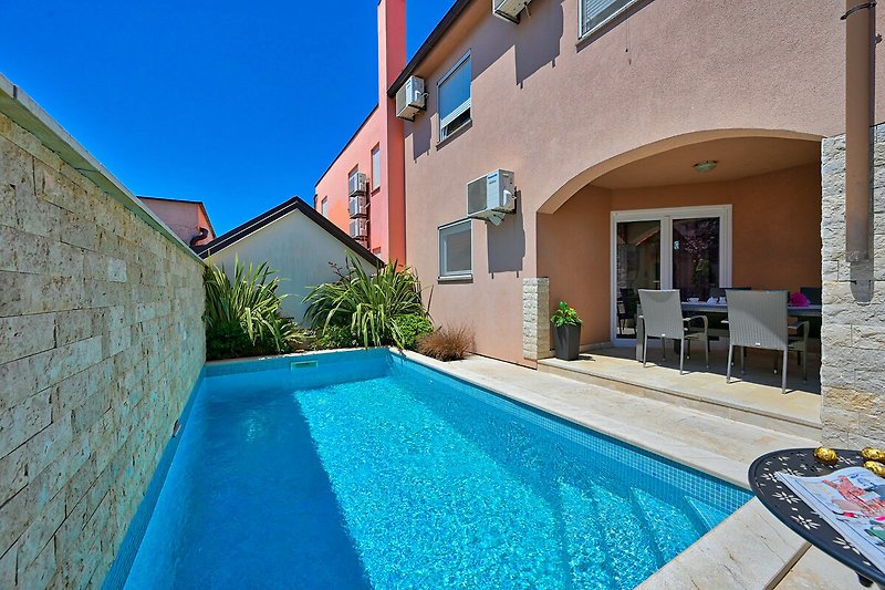 Schwimmbad mit azurblauem Wasser, umgeben von Pflanzen und einem blauen Himmel.