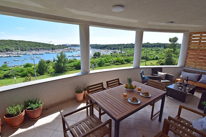 Großer Balkon mit Holzmöbeln und grünen Pflanzen.