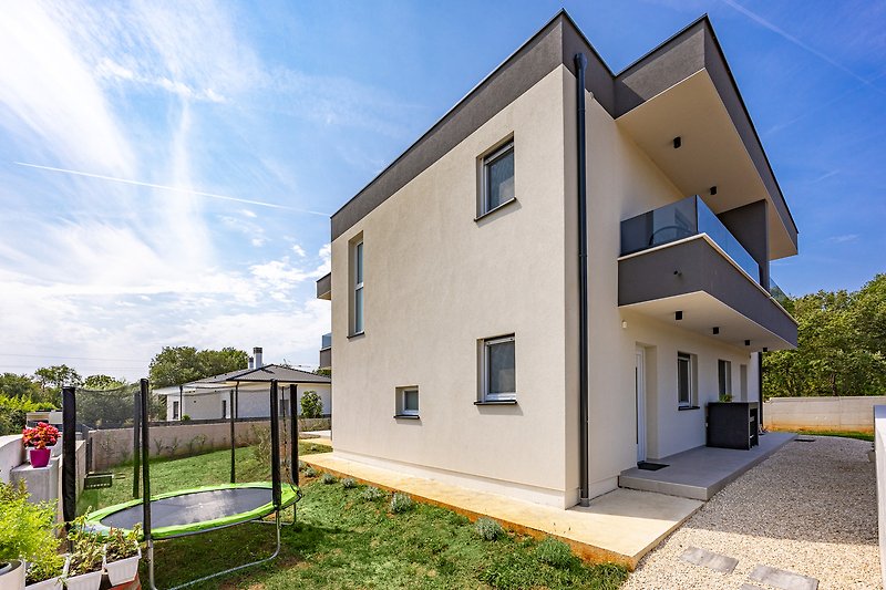 Modernes Haus mit Garten, Bäumen und blühenden Pflanzen.