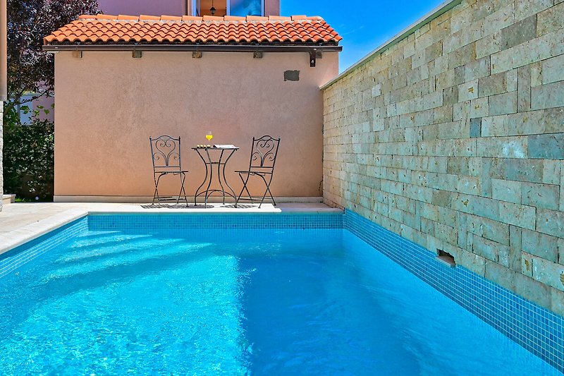 Schwimmbad mit azurblauem Wasser, umgeben von Pflanzen und einem blauen Himmel.