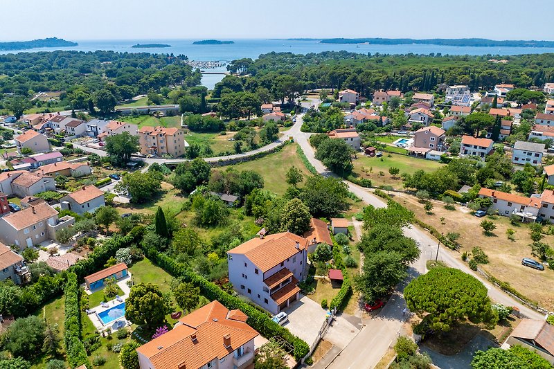 Luftaufnahme: Haus mit Garten, Bäumen und Blick auf die Stadt.