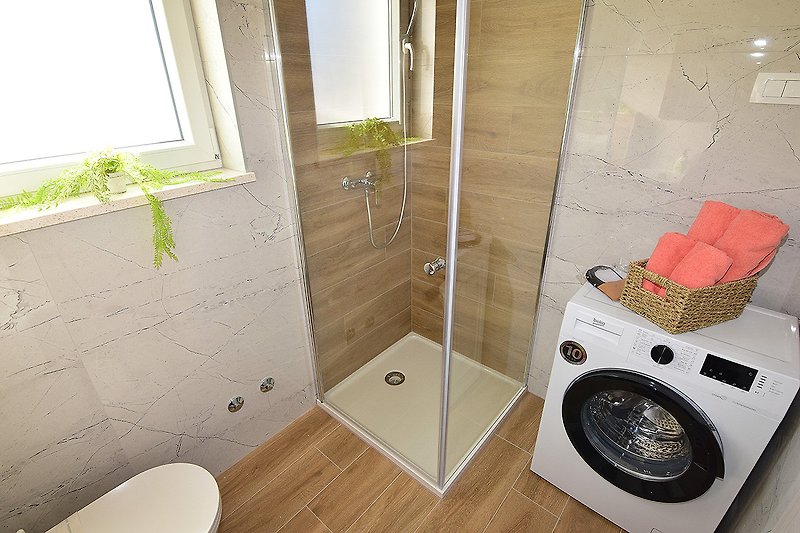 Modernes Badezimmer mit Glasdusche, Spiegel und Pflanze.