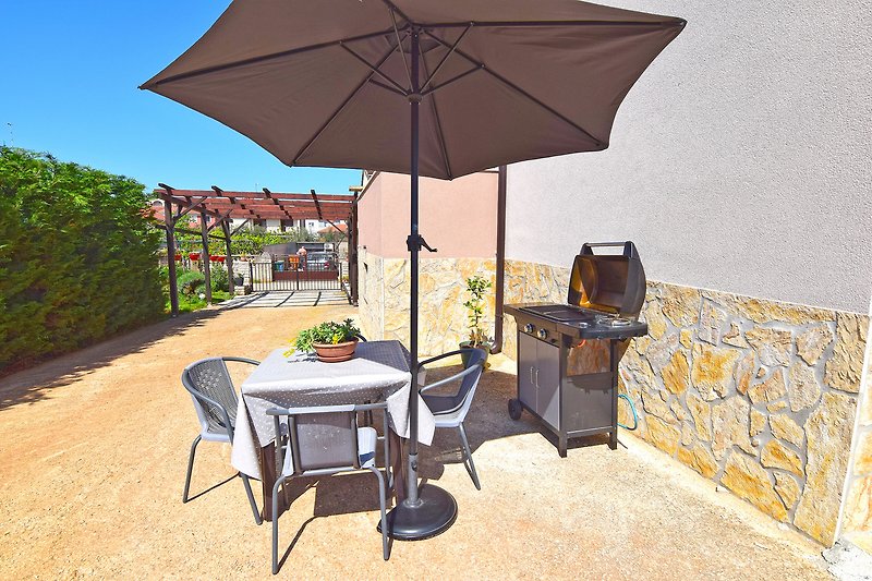 Sonniger Außenbereich mit Tisch, Stühlen und Sonnenschirm.