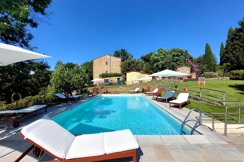 Villa mit Pool, Sonnenliegen und Gartenmöbeln im Freien.