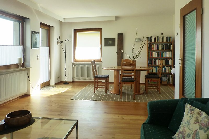 Gemütliches Wohnzimmer mit Holzboden, bequemer Couch, Sessel, Tisch mit 4 Stühlen, Zugang zur Terrasse.