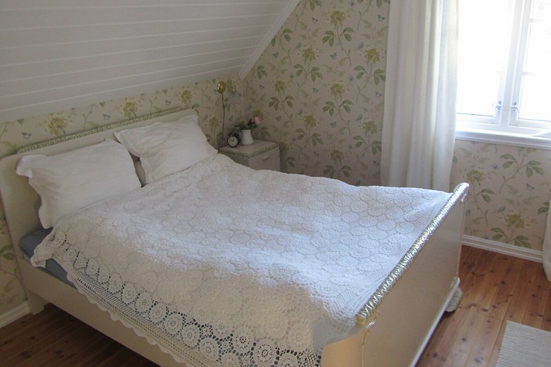 Gemütliches Schlafzimmer mit Holzbett, Fensterbehang und gemütlicher Einrichtung.