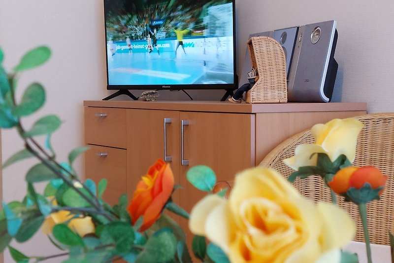Blumiges Wohnzimmer mit Fernseher und Musikinstrument. Gemütliche Floristik.