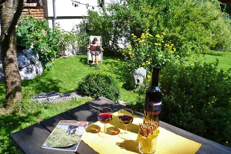 Einladender Garten mit grünem Rasen, Tisch, Stühlen und Wein.