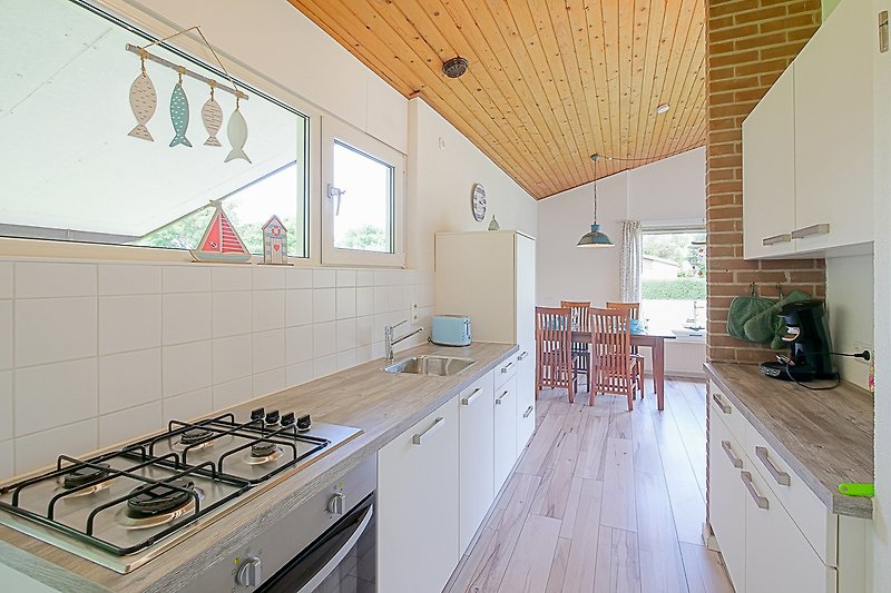 Küche mit Holzschränken, Gasherd und Fenster.