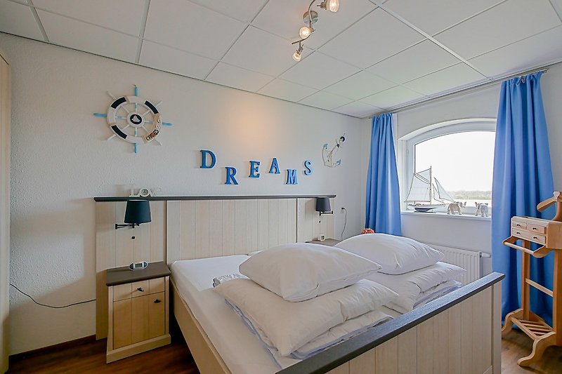 Schlafzimmer mit blauem Bett, Holzmöbeln und Lampen.