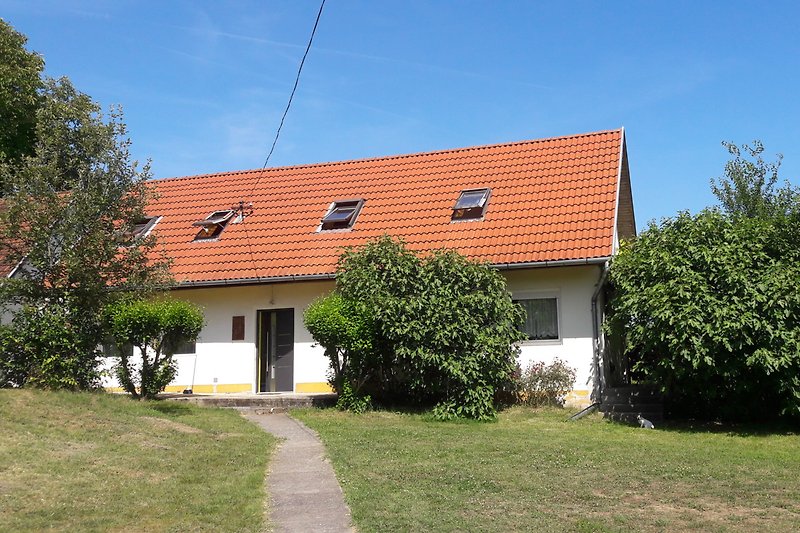 Charmantes Haus mit grünem Rasen, Bäumen und Sträuchern.