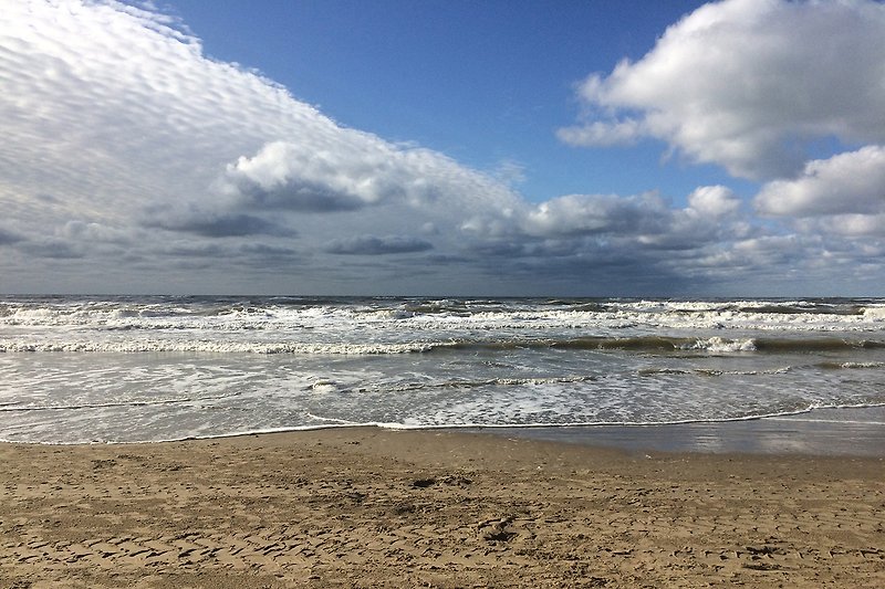 Strand mit Felsen, Wellen und blauem Himmel.