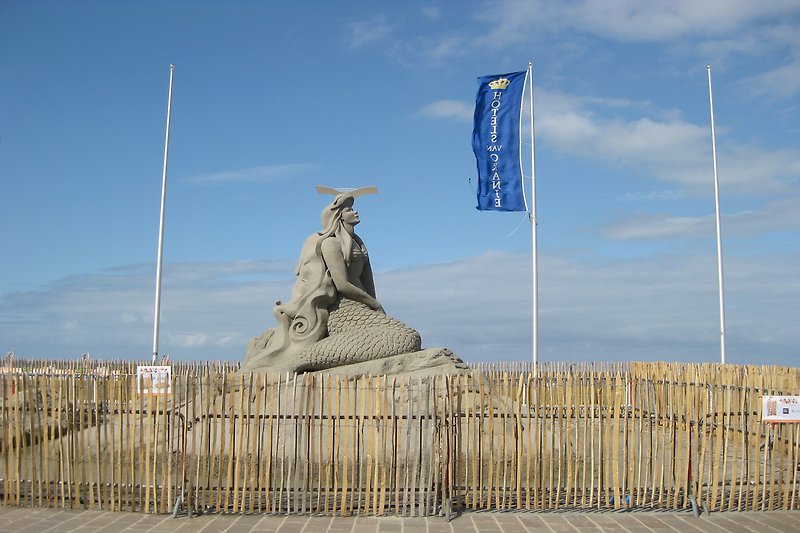Monumentale Statue vor blauem Himmel und grüner Landschaft.