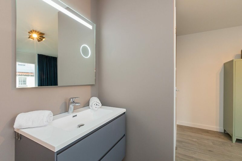 Badezimmer mit Spiegel, Waschbecken, Schrank und Armatur.
