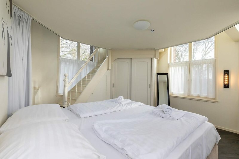 Schlafzimmer mit Holzbett, Kissen, Fenster und Vorhängen.
