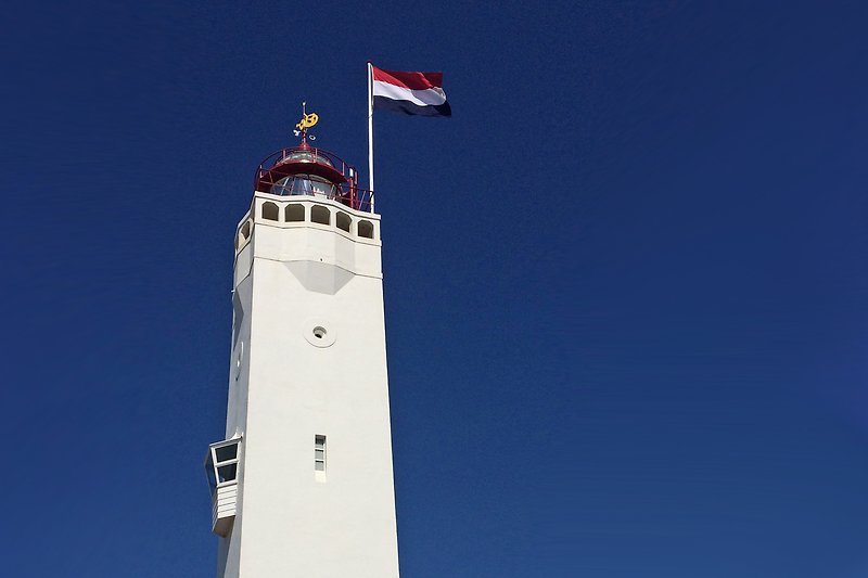 Leuchtturm mit Flagge und blauem Himmel.