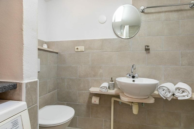 Badezimmer mit lila Akzenten, Spiegel, Waschbecken und Armatur.