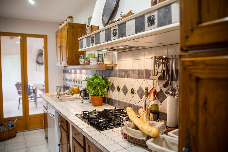 Küche mit provenzalischen Schränken und Flügeltür zur großen überdachten Terrasse mit Esstisch (Cuisine d'été)