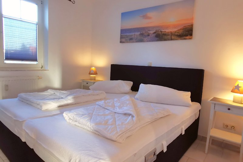Schlafzimmer mit Fenster und bequemem 180 x 200 cm Bett, gemütlicher Beleuchtung und Holzmöbeln.