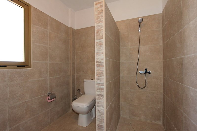 Badezimmer mit Dusche, Toilette und Waschbecken in Holzoptik.