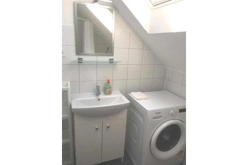 Badezimmer mit Waschmaschine, Spiegel und Waschbecken.