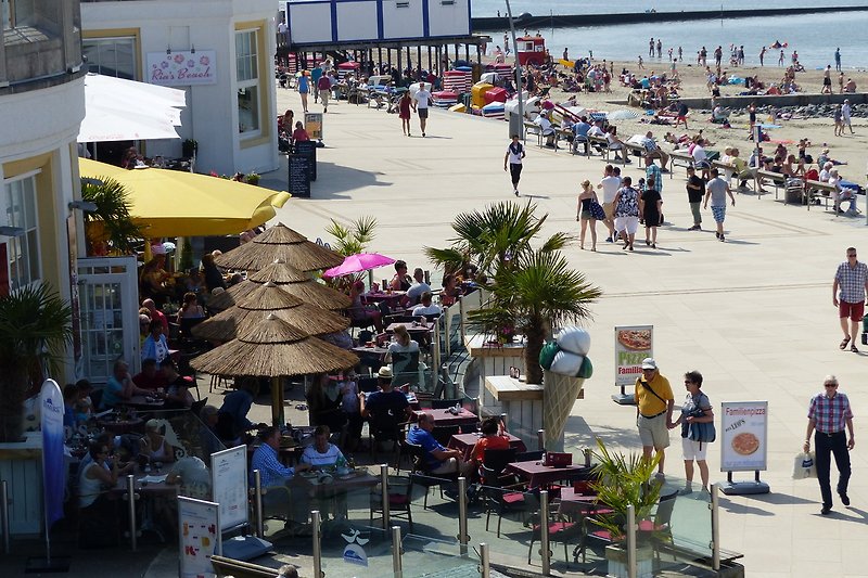 Sommerliche Strandpromenade mit Straßencafés und Einkaufsmöglichkeiten.