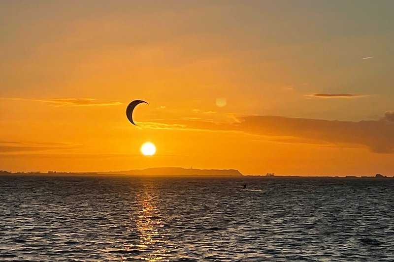 Ein atemberaubender Sonnenuntergang über dem See mit einem Paraglider am Himmel.