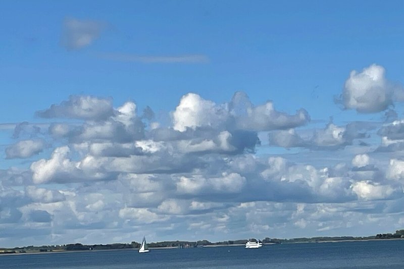 Blauer Himmel, Wolken und Boote auf ruhigem Meer.