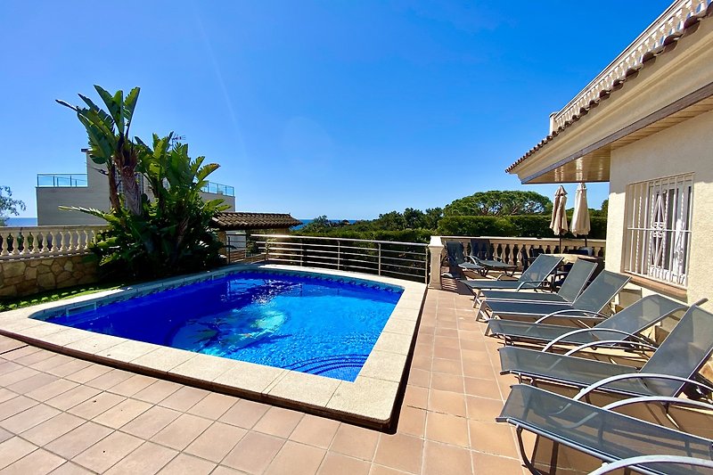 Luxuriöses Anwesen mit Pool, Sonnenliegen und grüner Landschaft.