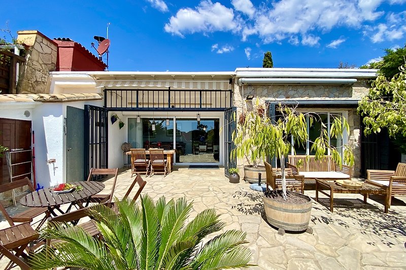 Villa mit Terrasse, Gartenmöbeln und blühenden Pflanzen.