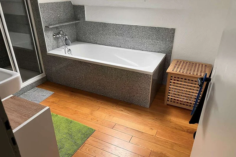 Helles Bad mit Holzdielen, Badewanne, Waschbecken und Tageslicht.