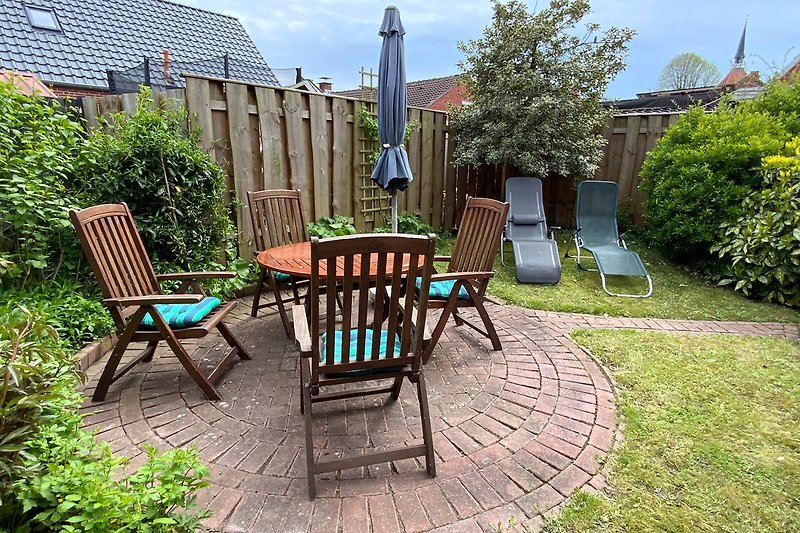 Eine idyllische Terrasse mit Gartenmöbeln und einem Baum im Hintergrund.