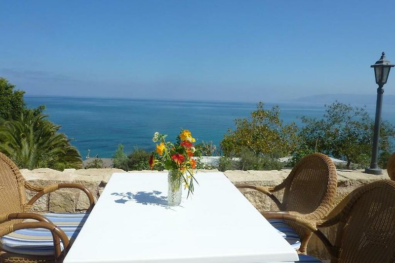Genießen Sie den Meerblick von der Terrasse dieses Ferienhauses mit blühenden Pflanzen und gemütlichen Möbeln.