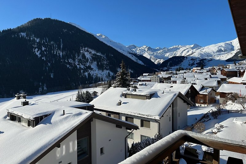 Winterliches Bergdorf mit schneebedeckten Gipfeln und Alpenblick.