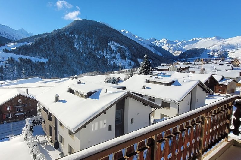 Winterliches Bergdorf mit schneebedeckten Häusern und Alpenpanorama.