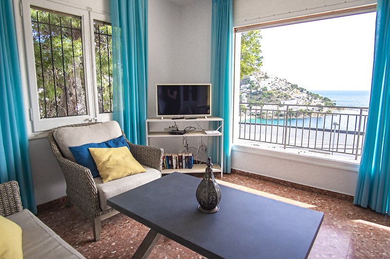 Wohnzimmer mit Holzmöbeln, blauer Vorhang, gemütlicher Couch und Fensterblick.