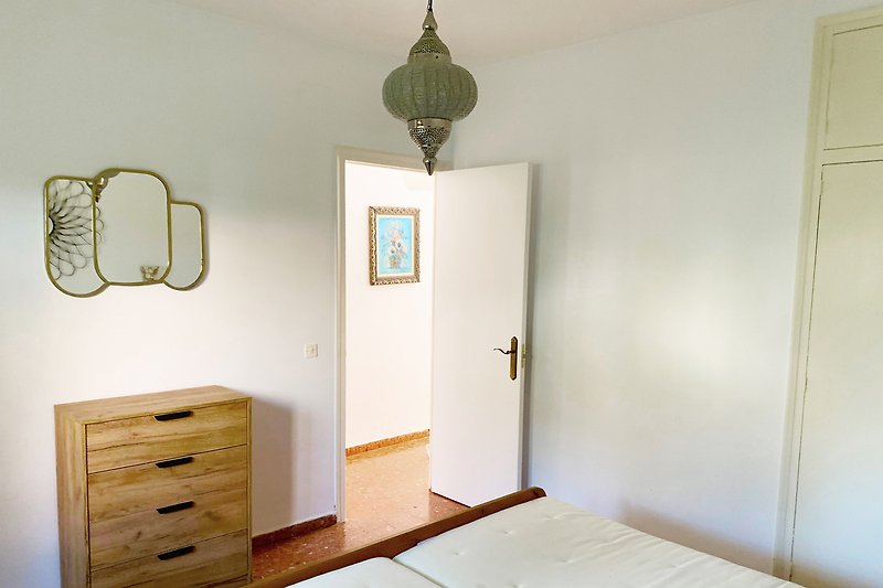 Schlafzimmer mit Holzmöbeln, Kommode, Bett und Fensterblick.