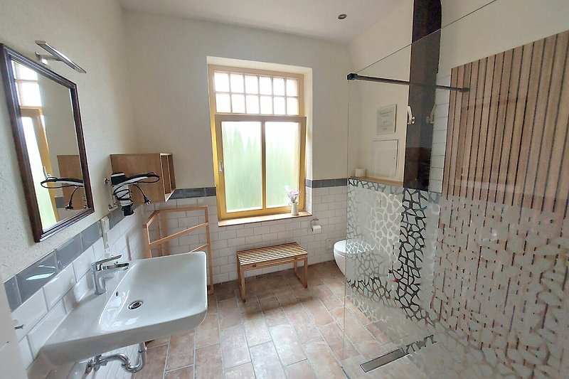 Ein helles Badezimmer mit Spiegel, Waschbecken und Fenster.
