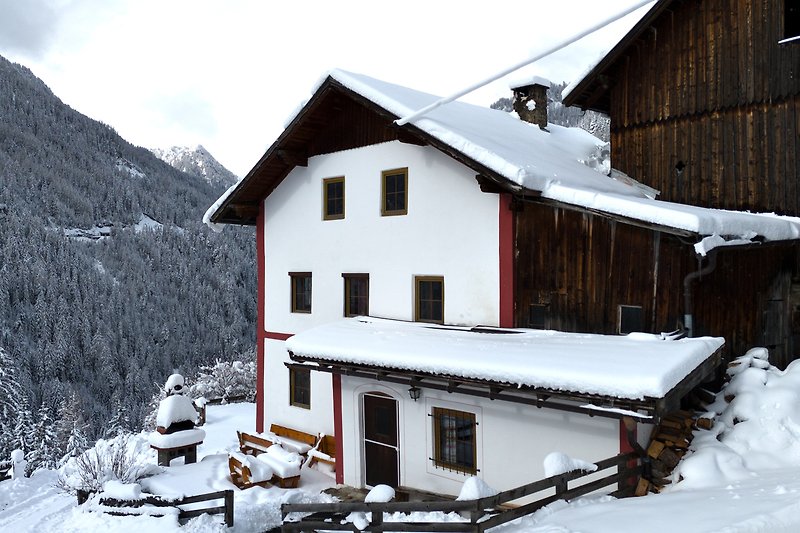 Winterliche Berghütte mit verschneiten Bäumen und Bergblick.