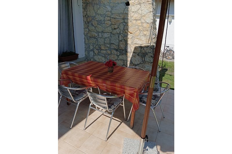 Gemütlicher Außenbereich mit Holztisch, Stühlen und Pflanzen.