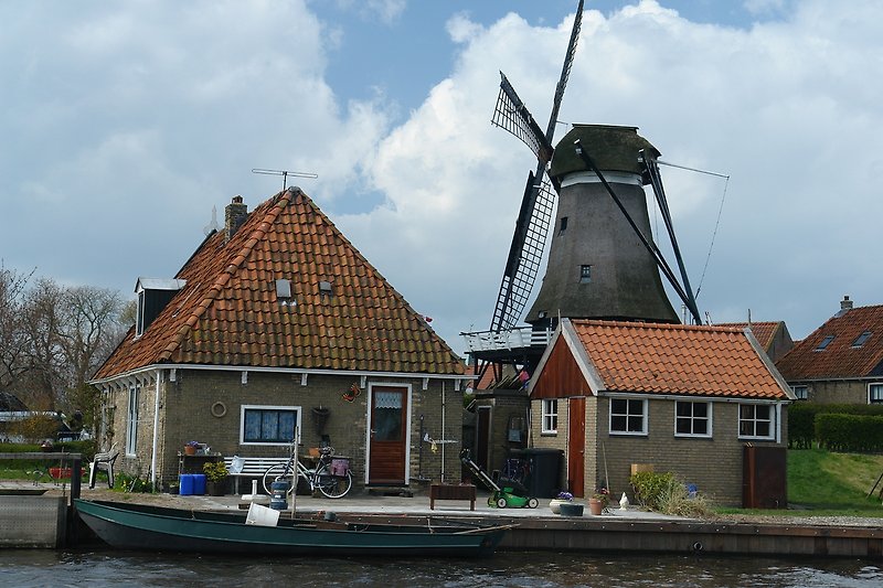 Windmühle am Kanal mit Booten und Bäumen.
