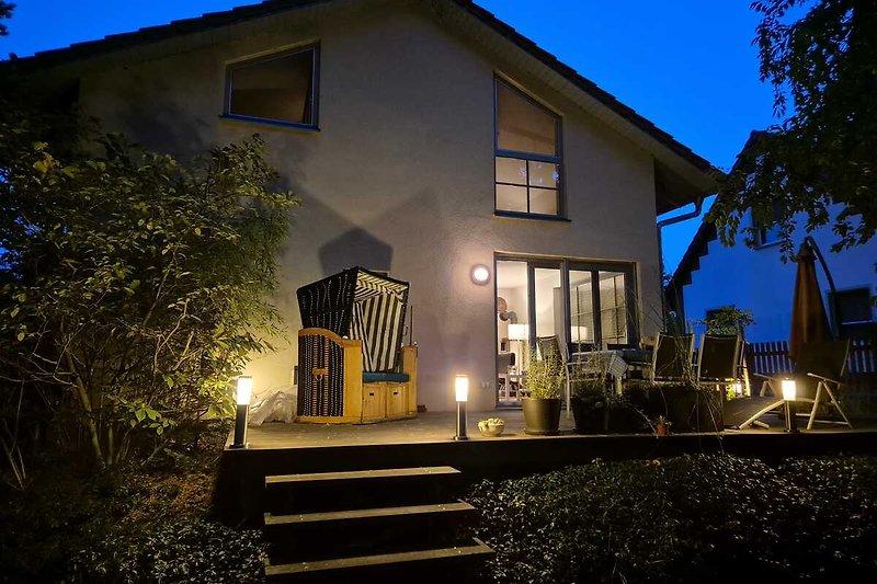 Historisches Haus mit beleuchtetem Garten und Holzveranda bei Nacht.