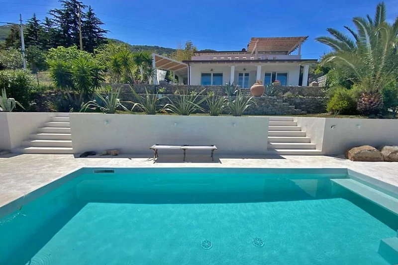 Schönes Haus mit Pool, umgeben von grüner Landschaft und Outdoor-Möbeln.