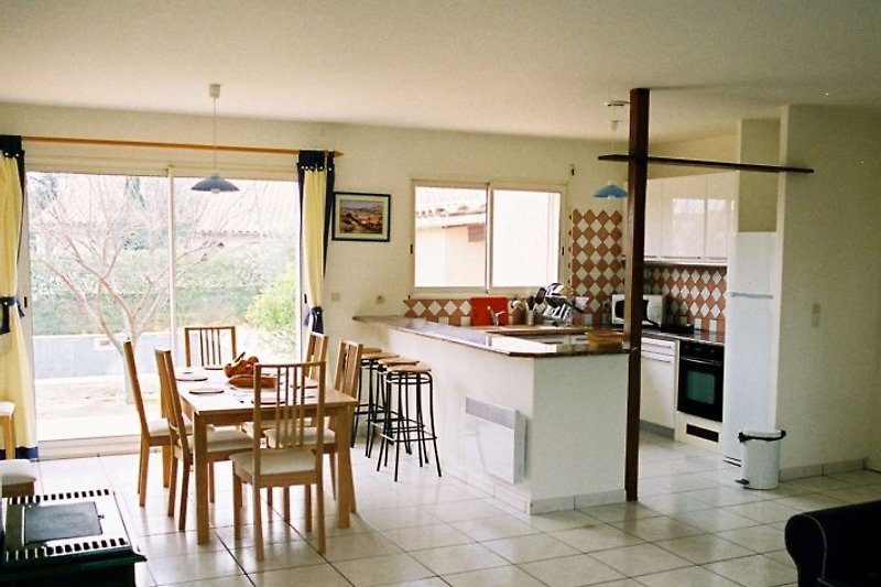 Cuisine moderne équipée avec un bar pour le petit déjeuner surmonté de granit, et une salle à manger avec des portes-fenêtres donnant sur la terrasse, la piscine et le jardin.