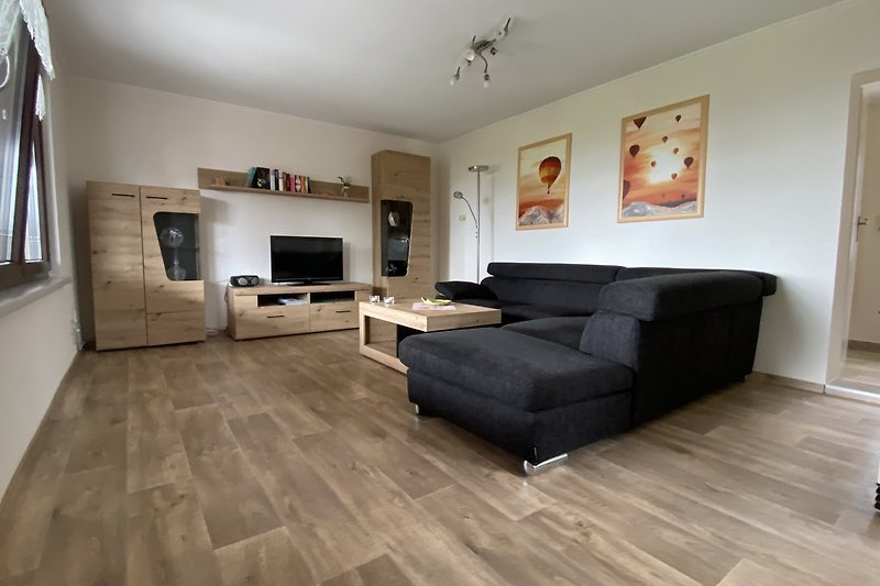 Gemütliches Wohnzimmer mit Holzboden, grauer Couch und Fenster.