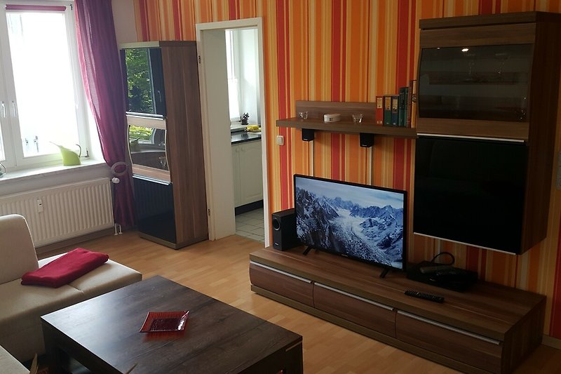 Wohnzimmer mit Fernseher, Couch, Tisch und Fenster.
