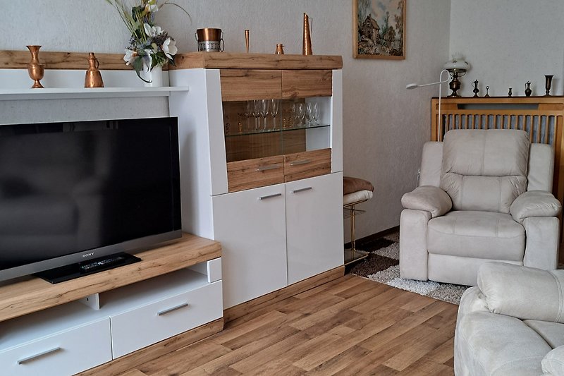 Modernes Wohnzimmer mit grauem Sofa, Holzregalen und großem Fernseher.