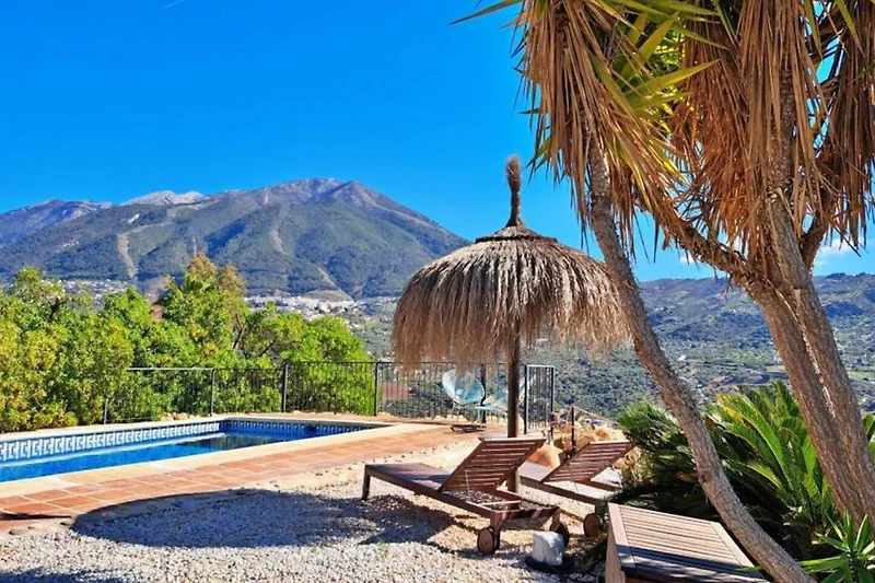 Pool mit Sonnenliegen, Schirmen und Blick auf Berge und viele exotische Pflanzen