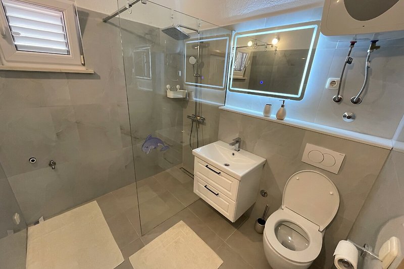 Modernes Badezimmer mit Spiegel, Fenster, Waschbecken und Toilette.
