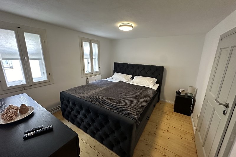 Gemütliches Schlafzimmer mit Holzbettrahmen und großen Fenstern.